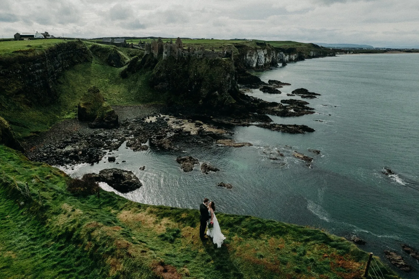 Aerial view of a couple on the Causeway Coast with Dunluce Castle beyond
